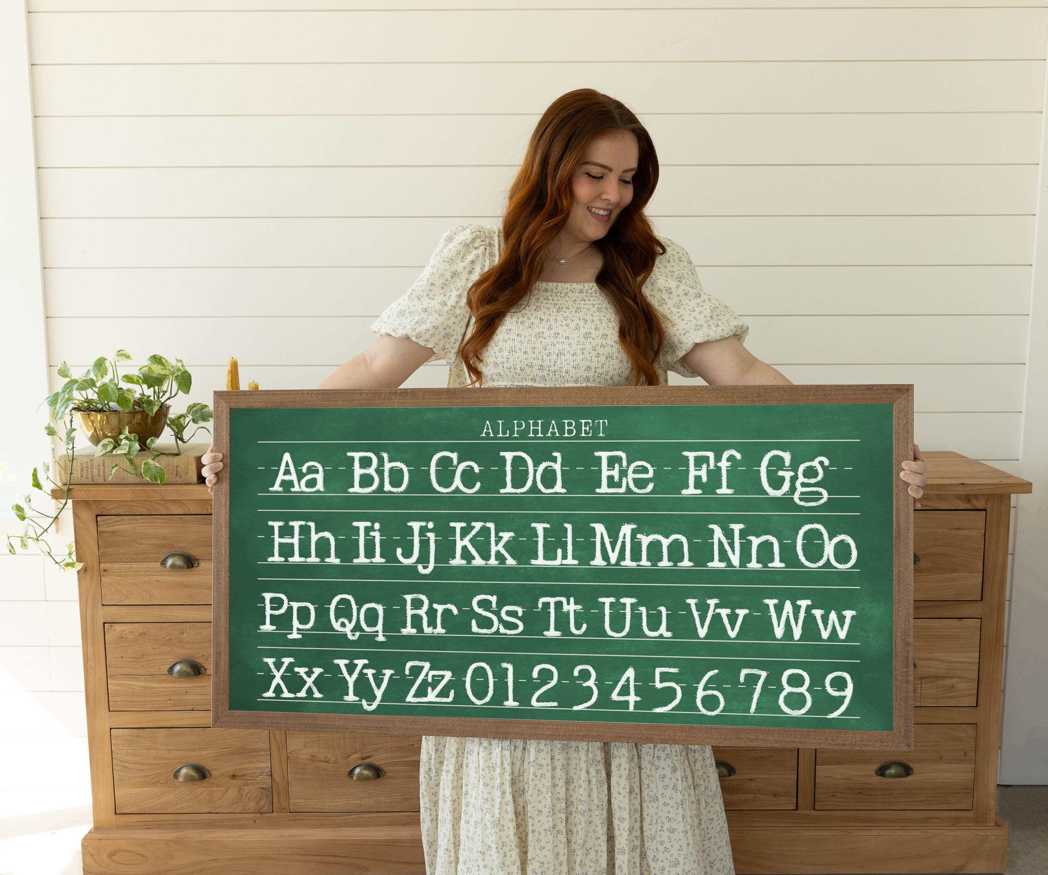 A woman is holding a large chalkboard with the alphabet written on it.