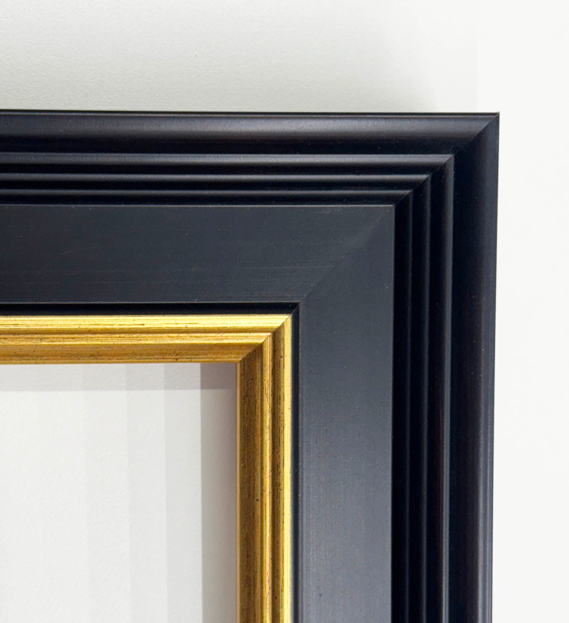 a close-up view of a black framed picture with a gold border, set against a white background.